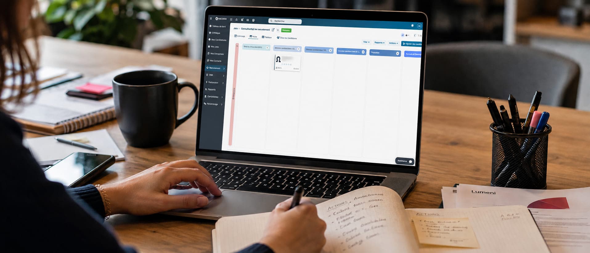 Un poste de travail de consultant en cours d’usage : l’ATS Nicoka ouvert sur un ordinateur portable, un carnet de notes, un téléphone et une tasse